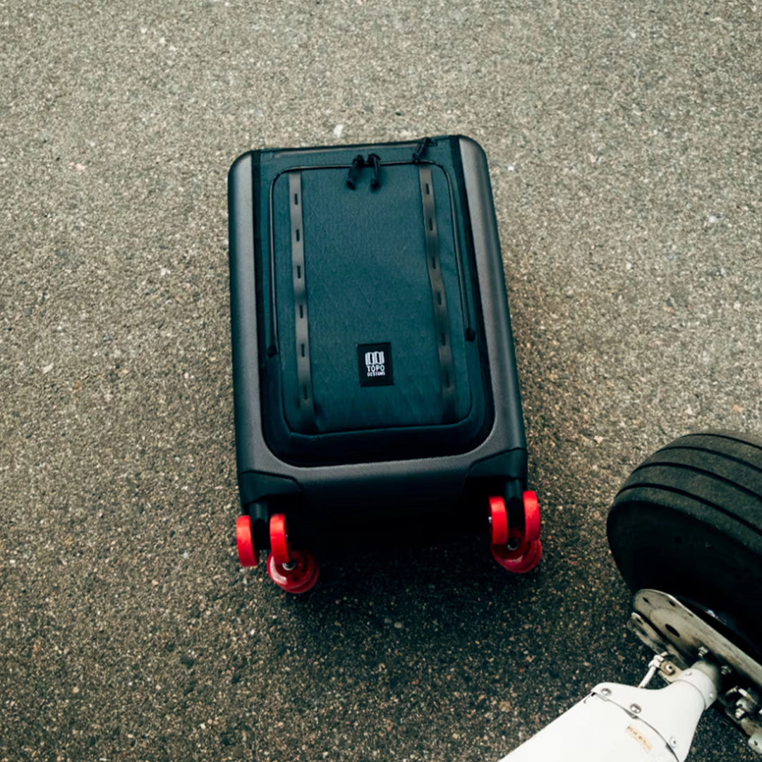 Topo Designs Global Pro Travel Roller shown outdoors on pavement with travel gear nearby